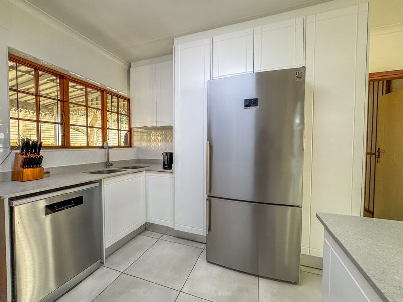 A functional kitchen featuring white cabinetry, laminate countertops, tiled flooring, and timber-framed windows, providing a clean and practical workspace.