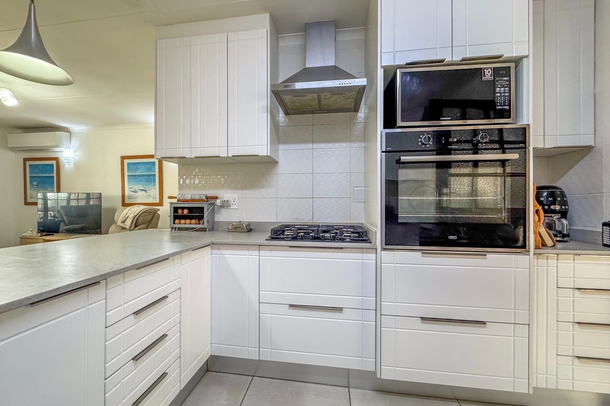 Modern kitchen featuring white cabinetry, stone countertops, gas hob, extractor fan, and integrated oven and microwave appliances.