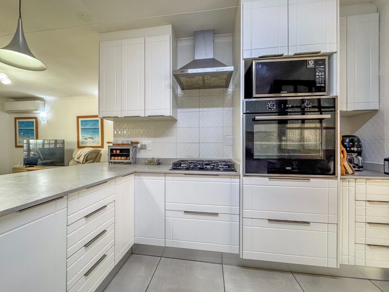 Modern kitchen featuring white cabinetry, stone countertops, gas hob, extractor fan, and integrated oven and microwave appliances.