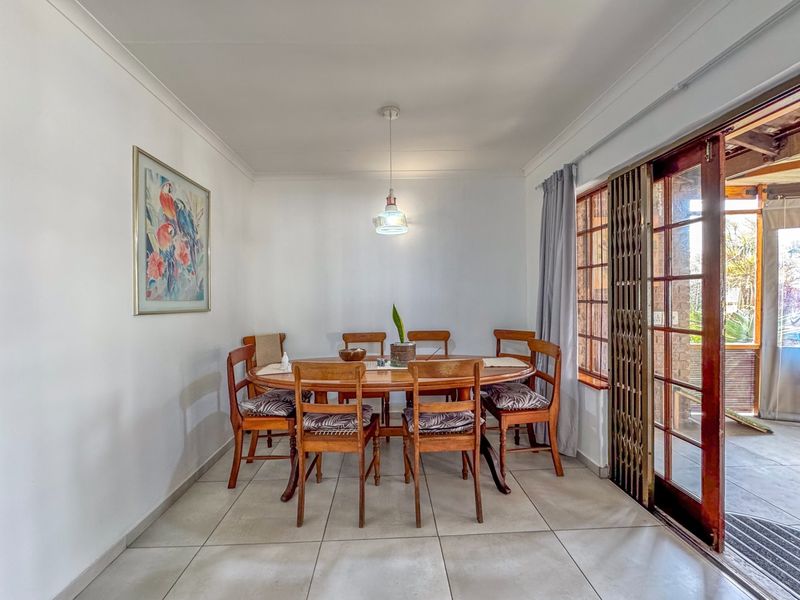 A bright dining room featuring neutral tiled flooring, a central pendant light, and a sliding glass door providing access to the outdoor patio area.