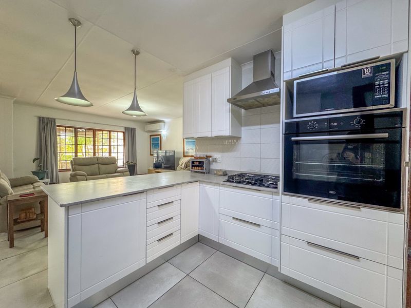 Modern open-plan kitchen featuring white cabinetry, integrated appliances, gas hob, and tiled flooring, seamlessly flowing into the adjacent living area.
