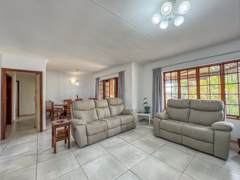 Open-plan living and dining area featuring neutral tiled flooring, large timber-framed windows, and a central ceiling light fixture.