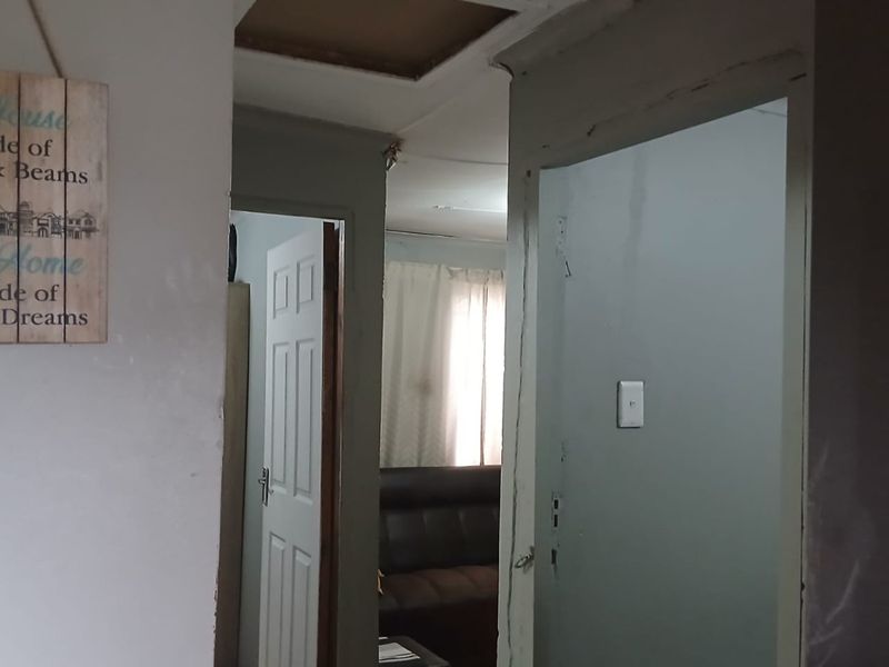 A narrow hallway showing signs of wear, including unfinished ceiling edges and damaged wall finishes, leading into an adjacent living space.