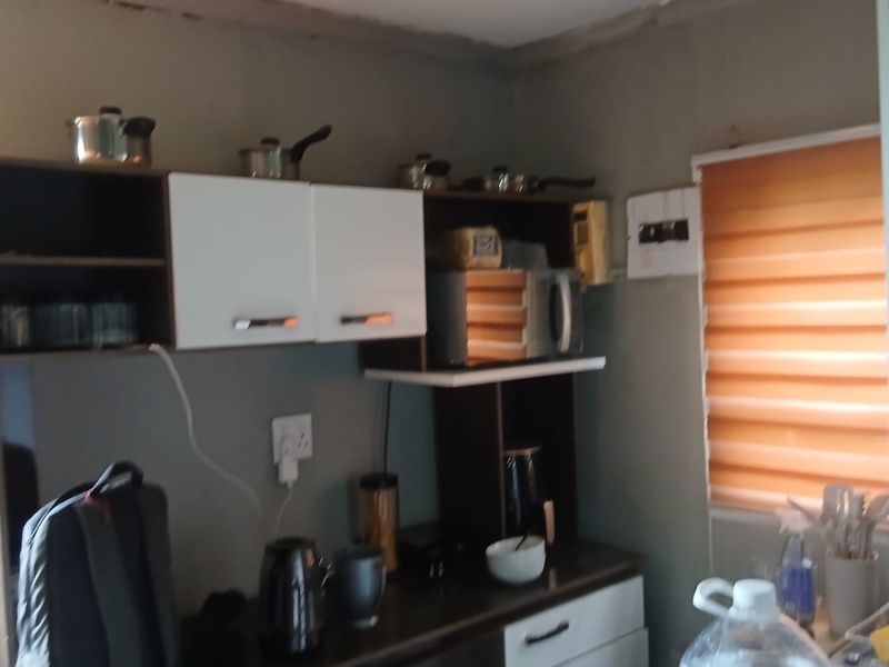 A compact kitchen area featuring built-in cabinetry, laminate countertops, and a dedicated microwave shelf, requiring minor cosmetic updates to the ceiling and walls.