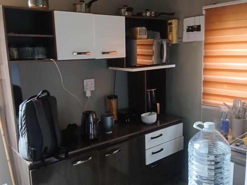 A compact kitchen area featuring modern two-tone cabinetry, laminate countertops, and functional roller blinds for light control.
