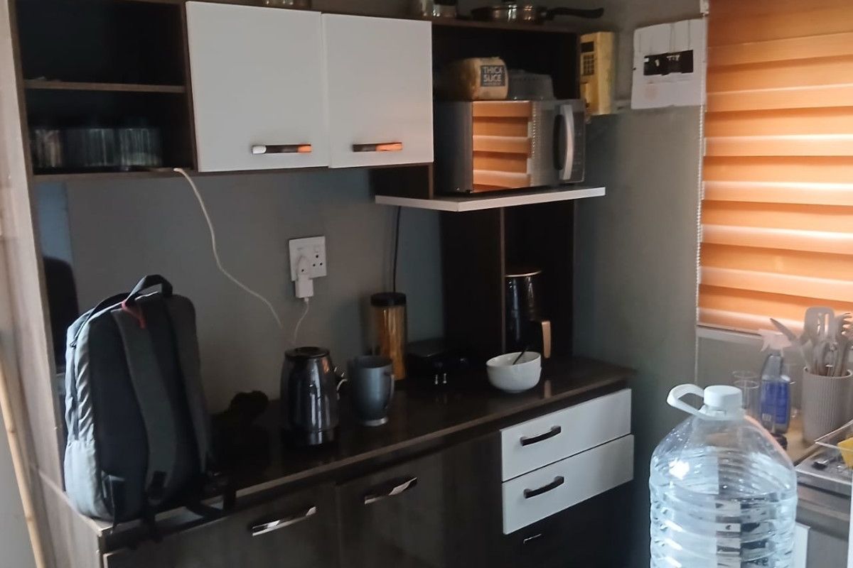 A compact kitchen area featuring modern two-tone cabinetry, laminate countertops, and functional roller blinds for light control.