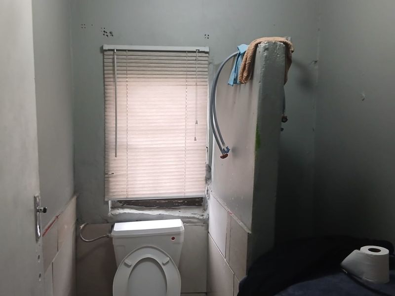 A small bathroom space featuring a toilet and window, currently requiring significant cosmetic updates and finishing of wall surfaces and plumbing fixtures.