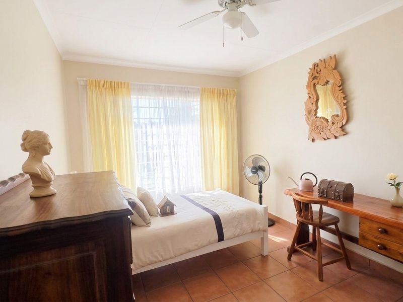 A bedroom featuring tiled flooring, a ceiling fan, and large windows fitted with security bars, offering a functional and well-lit living space.