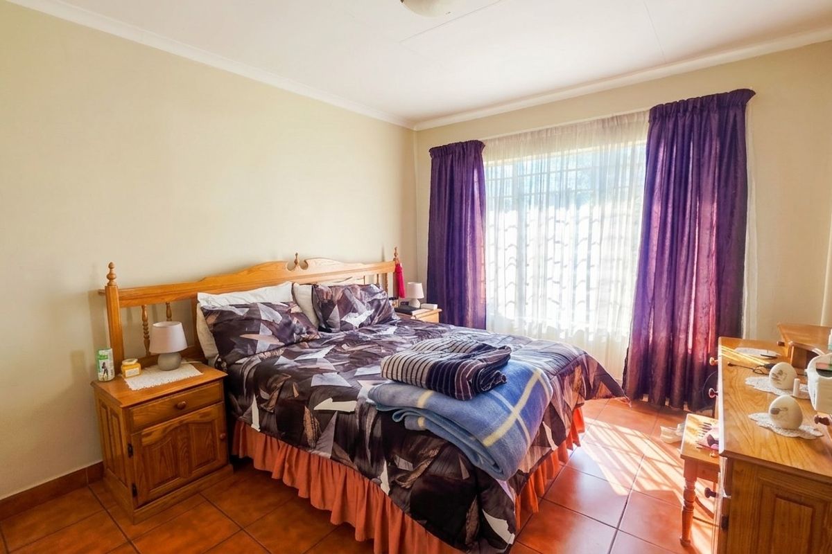 A well-lit bedroom featuring tiled flooring and large windows with curtain rails, offering a functional and comfortable living space.