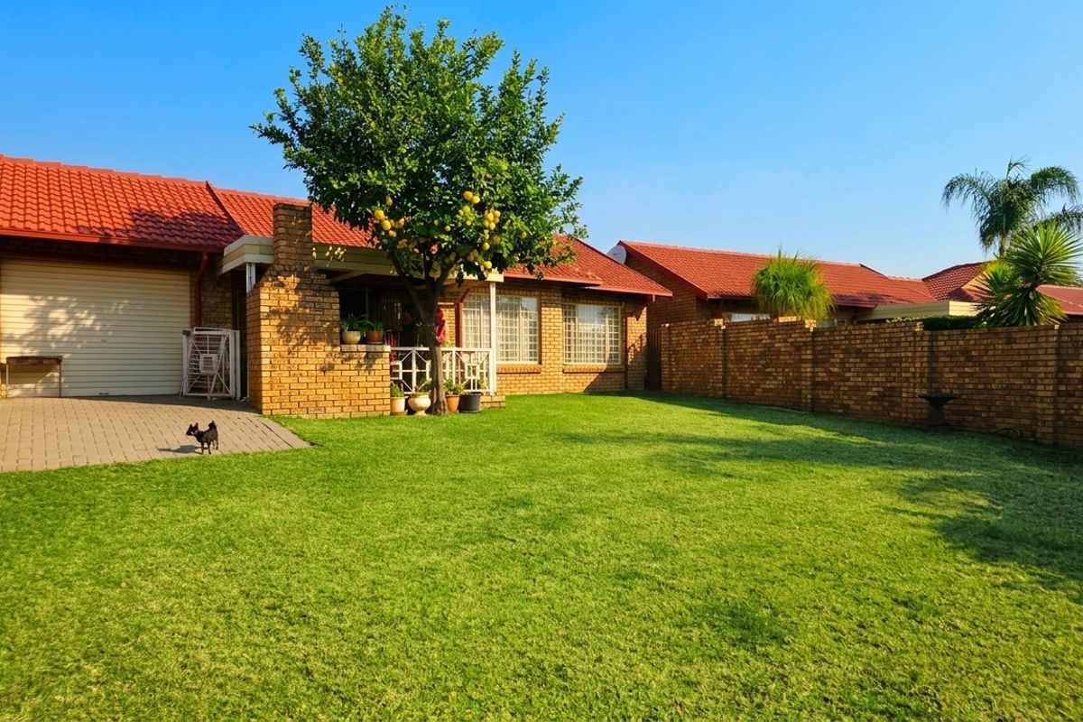 Rear view of the townhouse featuring a spacious private garden, brick boundary walls, paved driveway, and a single garage.