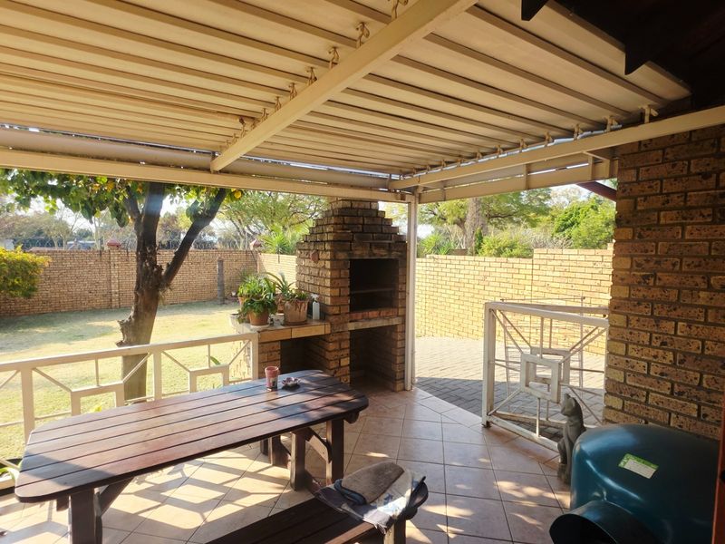 Covered outdoor patio featuring a built-in brick braai, tiled flooring, and direct access to the rear garden and paved area.