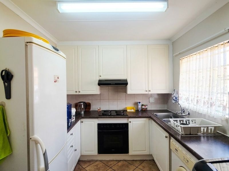 A functional kitchen featuring white cabinetry, dark laminate countertops, a built-in oven with hob, and tiled splashbacks, offering a clean and practical workspace.