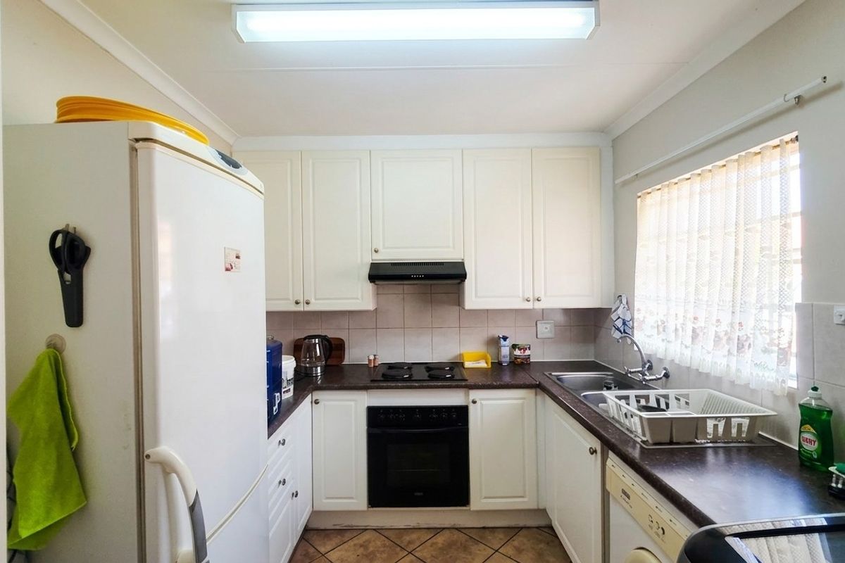 A functional kitchen featuring white cabinetry, dark laminate countertops, a built-in oven with hob, and tiled splashbacks, offering a clean and practical workspace.