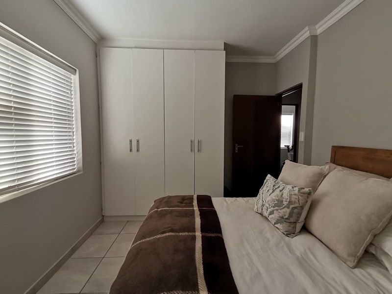 A well-maintained bedroom featuring built-in cupboards, tiled flooring, and venetian blinds, offering a clean and functional living space.