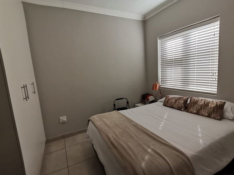 A well-maintained bedroom featuring neutral wall tones, tiled flooring, built-in cupboards, and venetian blinds for privacy.