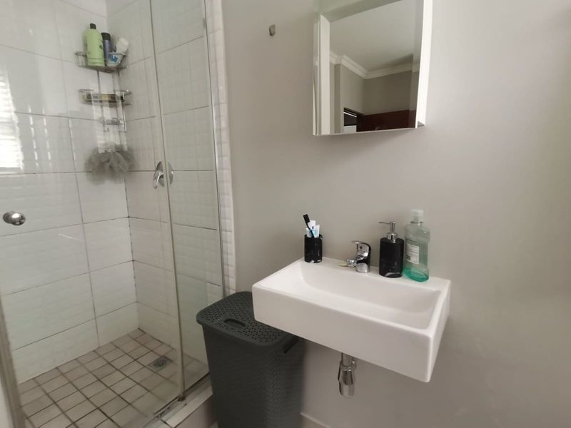 A functional bathroom featuring a glass-enclosed shower and a modern wall-mounted basin with a mirrored medicine cabinet.
