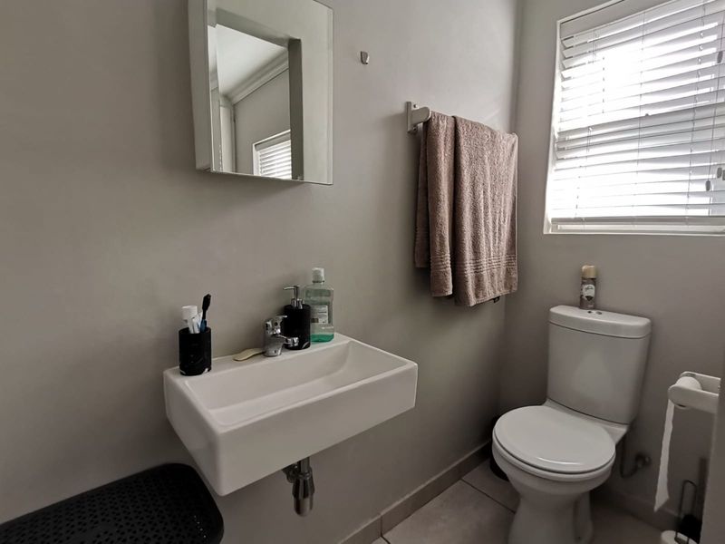 A functional bathroom featuring a wall-mounted basin, chrome fixtures, a toilet, and a medicine cabinet with neutral wall finishes.