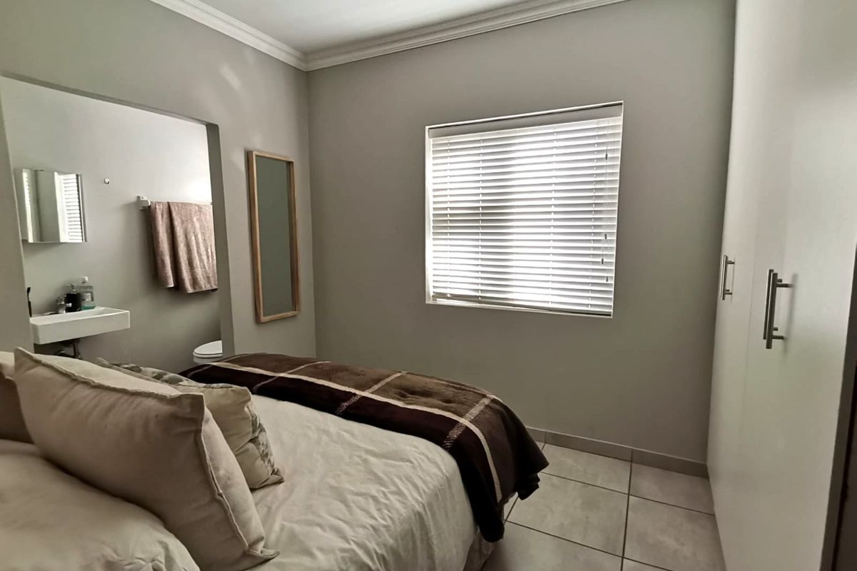 A well-maintained bedroom featuring built-in cupboards, tiled flooring, and an en-suite bathroom with a wall-mounted basin.