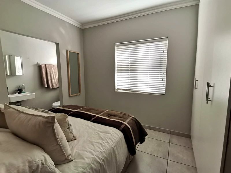 A well-maintained bedroom featuring built-in cupboards, tiled flooring, and an en-suite bathroom with a wall-mounted basin.