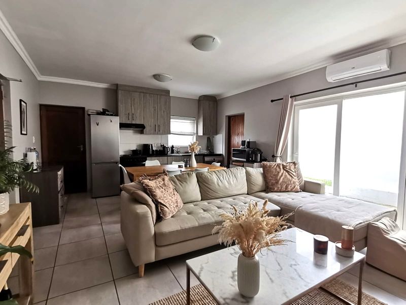 Open-plan living and kitchen area featuring tiled floors, modern cabinetry, and sliding glass doors leading to the exterior, complemented by a wall-mounted air conditioner.