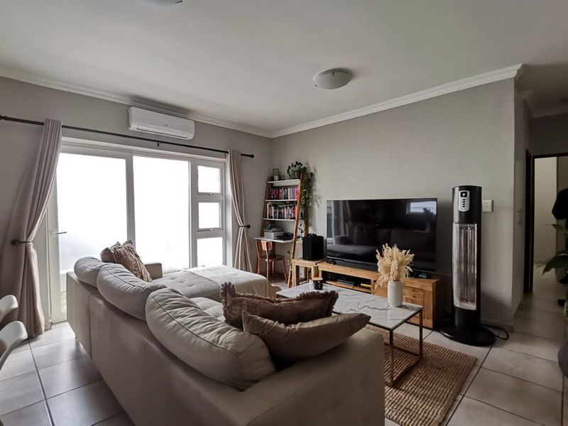 A well-lit living room featuring tiled flooring, a wall-mounted split-system air conditioner, and large sliding glass doors providing natural light.
