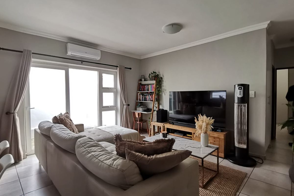 A well-lit living room featuring tiled flooring, a wall-mounted split-system air conditioner, and large sliding glass doors providing natural light.