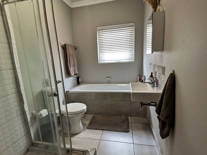 A functional bathroom featuring a shower enclosure, built-in bathtub, wall-mounted basin, and tiled flooring with neutral finishes.