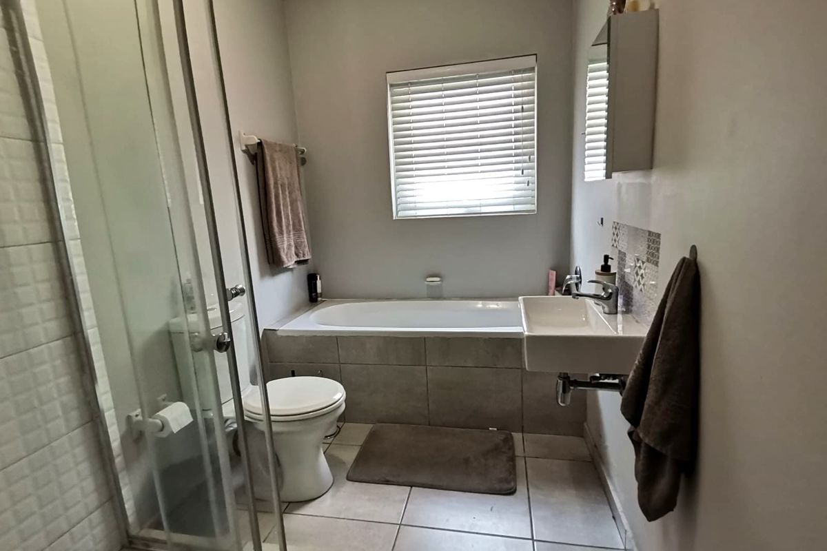 A functional bathroom featuring a shower enclosure, built-in bathtub, wall-mounted basin, and tiled flooring with neutral finishes.