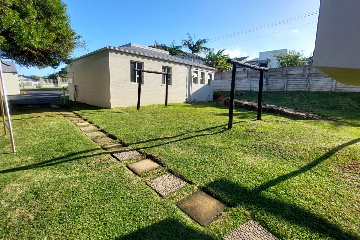 A rear garden area featuring a lawn, a stepped stone pathway, and a painted brick exterior wall with perimeter security fencing.