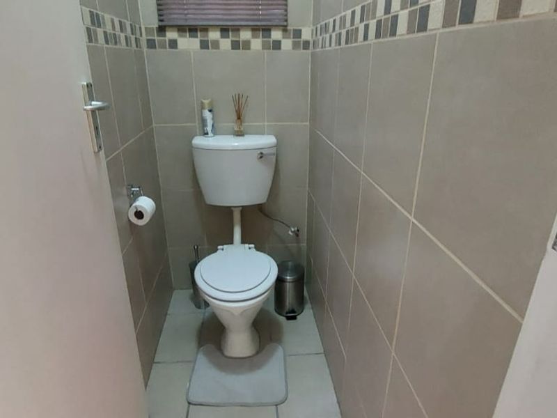 A compact guest bathroom featuring neutral ceramic wall and floor tiles with a decorative mosaic border.