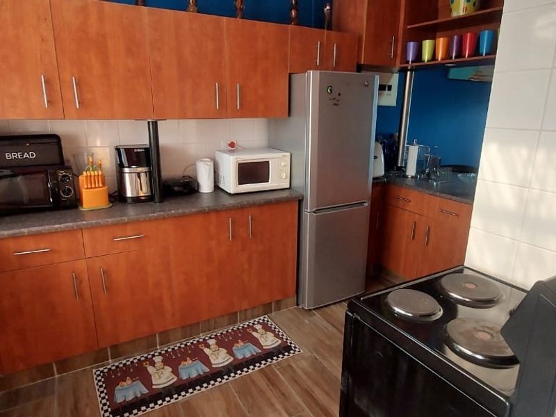 A functional kitchen featuring wood-look laminate cabinetry, dark countertops, a stainless steel sink, and a freestanding electric stove with tiled splashback.