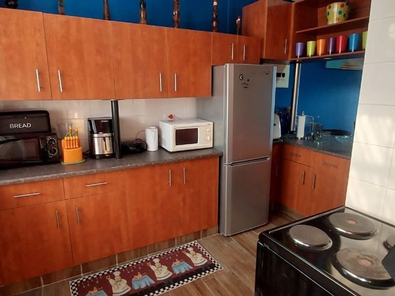 A functional kitchen featuring wood-look laminate cabinetry, dark countertops, a tiled splashback, and a freestanding electric stove.