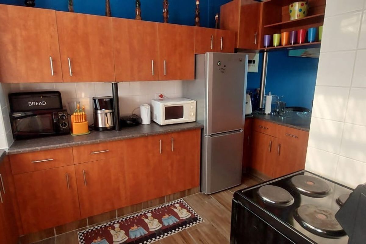 A functional kitchen featuring wood-look laminate cabinetry, dark countertops, a tiled splashback, and a freestanding electric stove.