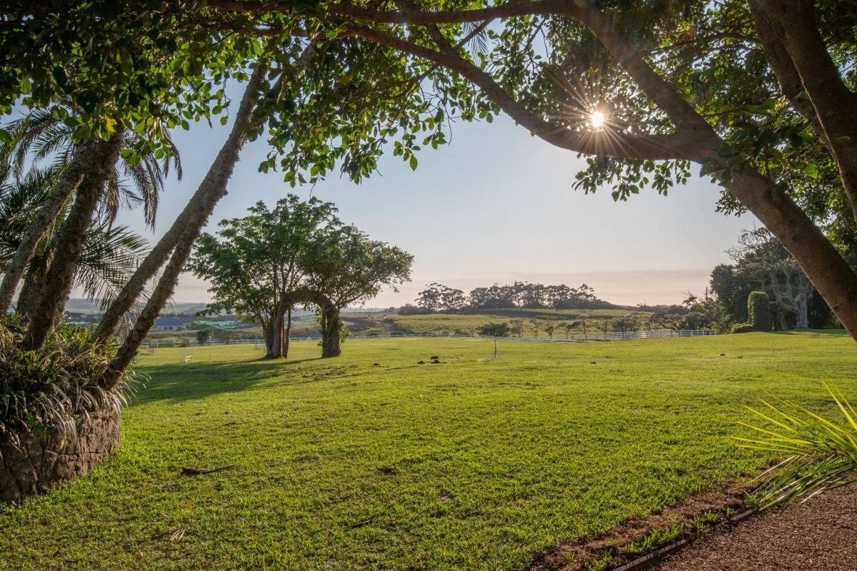 A spacious, well-maintained grassy garden area featuring mature trees and white perimeter fencing, offering a peaceful and open outdoor setting.