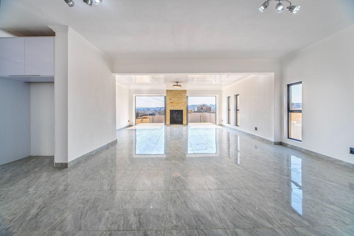 Spacious, open-plan living area featuring polished tiled floors, a central stone-clad fireplace, and large sliding doors leading to an outdoor space.