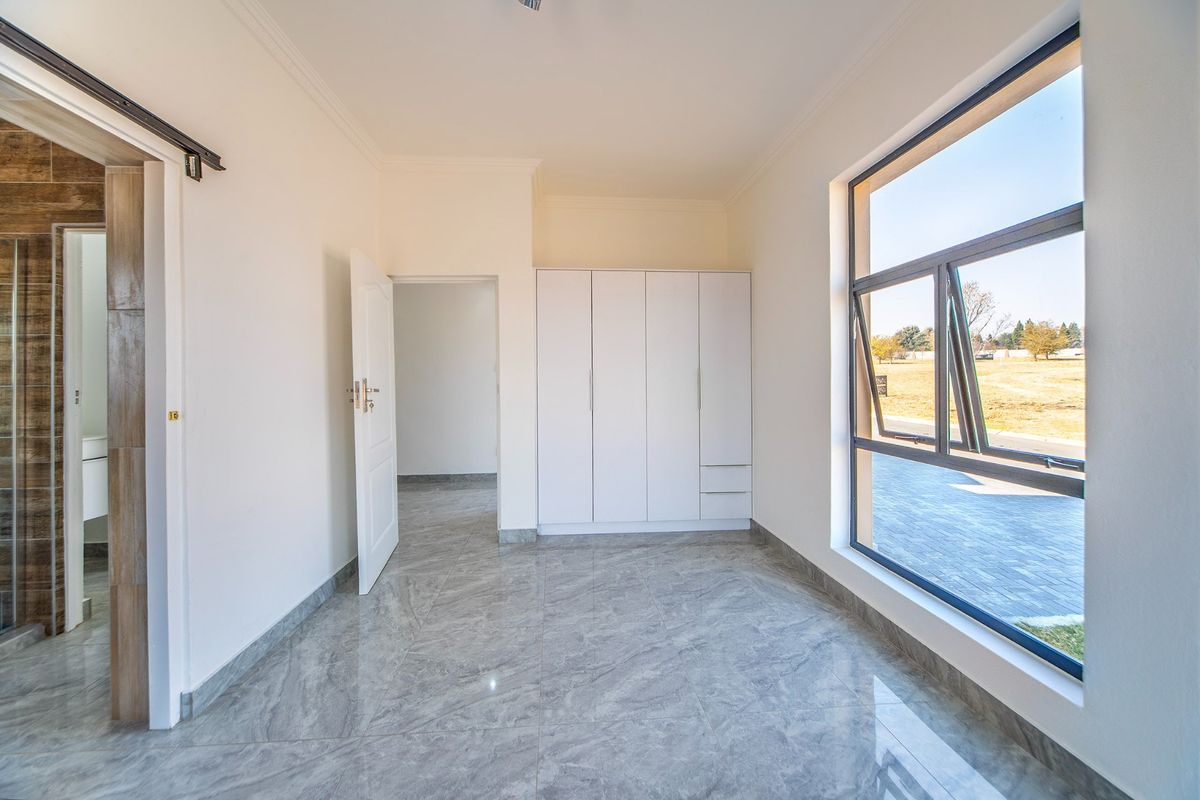 A bright, modern bedroom featuring neutral walls, large windows, built-in wardrobes, and sleek grey tiled flooring, offering a clean and versatile living space.