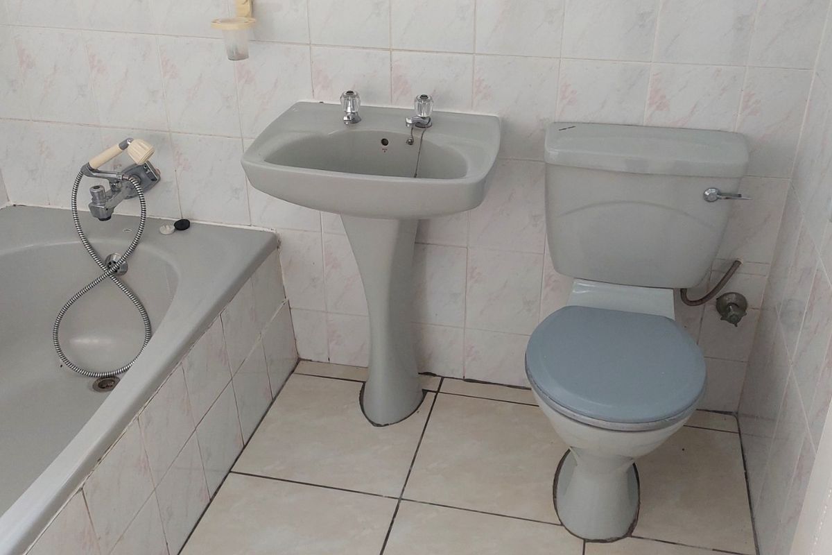 A functional bathroom featuring a pedestal basin, toilet, and bathtub with wall and floor tiling, presenting an opportunity for modern renovation.