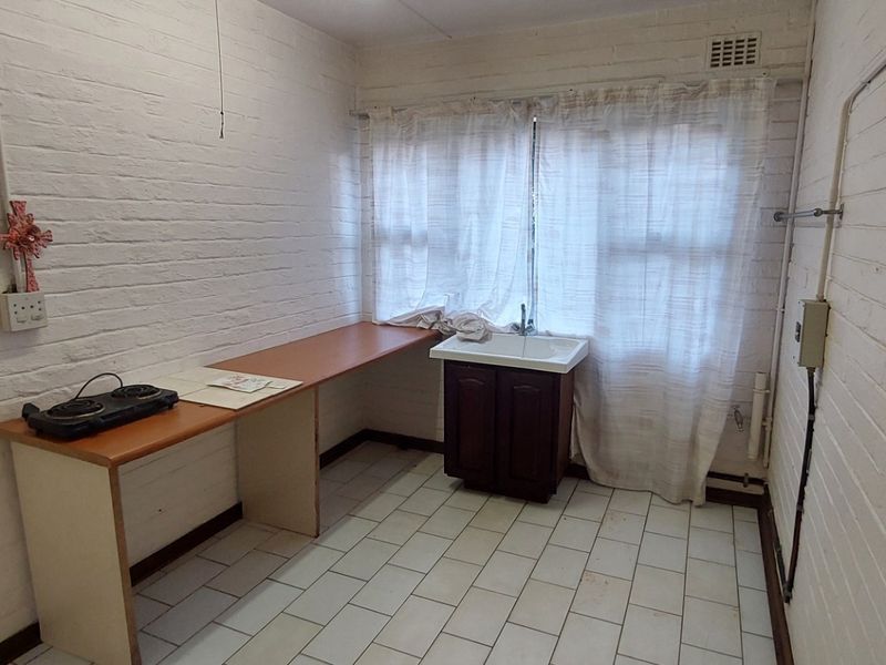 A functional scullery or utility area featuring exposed brick walls, tiled flooring, a built-in sink, and a laminate workspace.