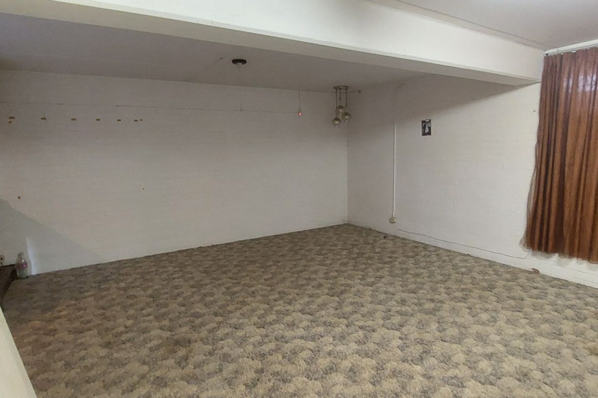 An empty, dated living room featuring a brick fireplace, carpeted flooring, and large window curtains, offering a blank canvas for renovation.