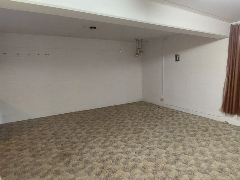 An empty, dated living room featuring a brick fireplace, carpeted flooring, and large window curtains, offering a blank canvas for renovation.