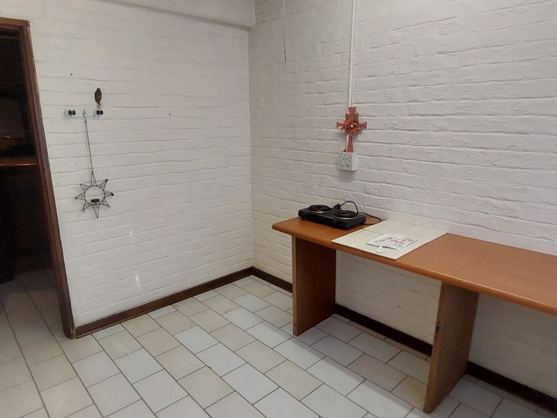 A basic kitchen area featuring white painted brick walls, tiled flooring, and a simple built-in wooden counter with an electric hob.