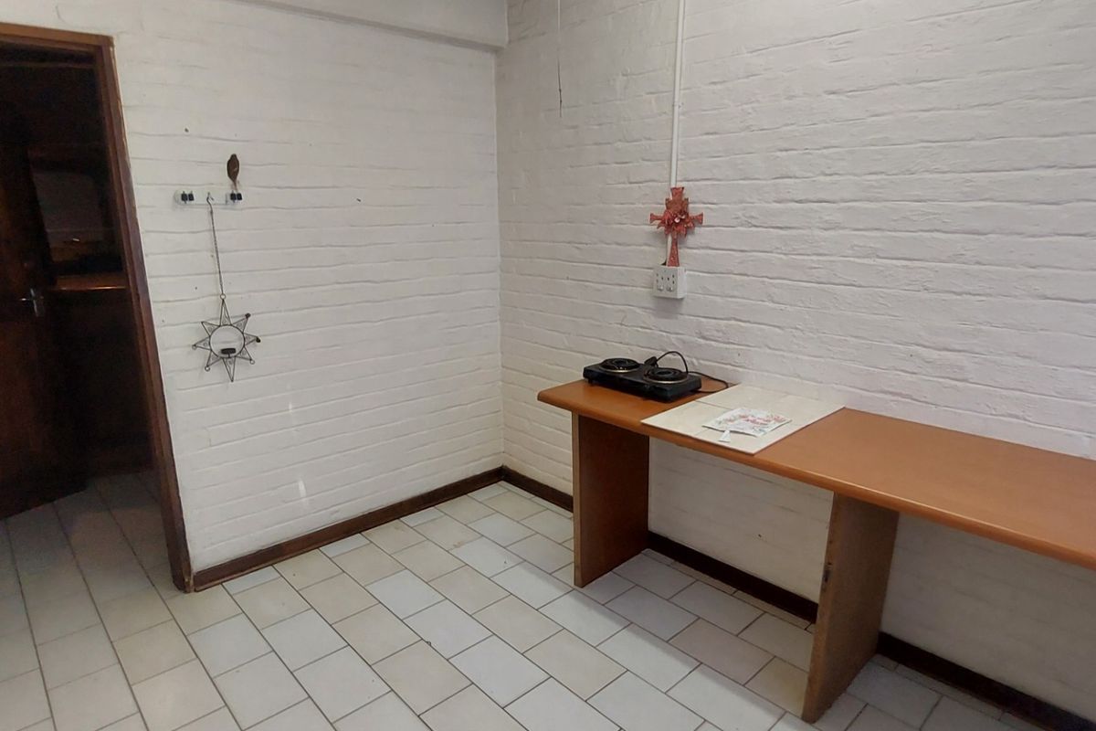 A basic kitchen area featuring white painted brick walls, tiled flooring, and a simple built-in wooden counter with an electric hob.