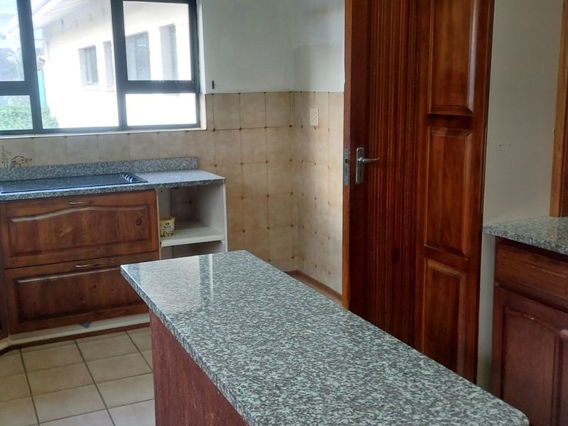 A functional kitchen featuring granite countertops, built-in oven, hob, and traditional wooden cabinetry with tiled backsplash and flooring.
