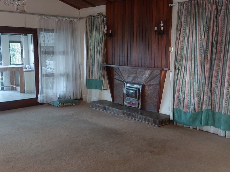 Spacious living room featuring a wood-burning fireplace with stone hearth, timber wall paneling, and sliding glass doors leading to an outdoor area.
