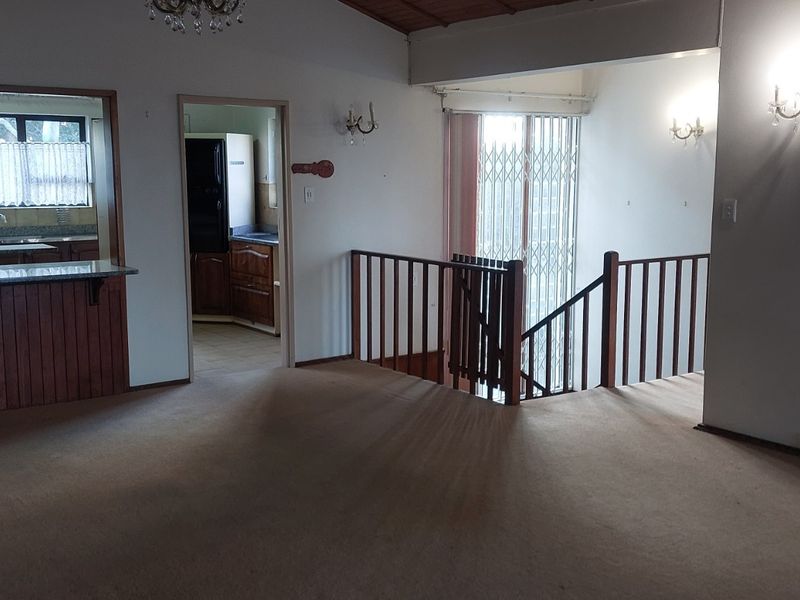 Spacious open-plan living area featuring a breakfast bar, kitchen access, and a wooden staircase with a security gate.