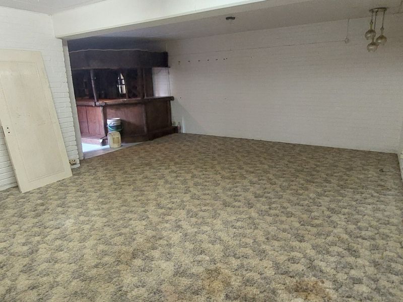 A spacious, empty room featuring a built-in bar area, painted brick walls, and carpet flooring, offering potential for a versatile entertainment space.