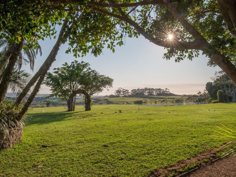 A scenic view of a well-maintained residential vacant land plot featuring mature trees, expansive green lawns, and white perimeter fencing.