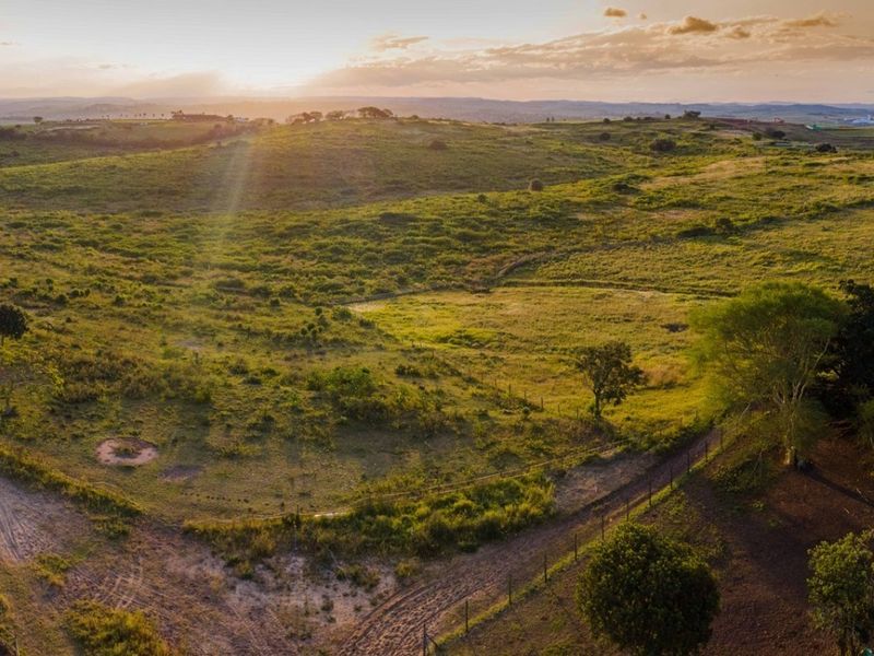 An aerial view of a large, undeveloped residential land parcel featuring rolling hills, natural vegetation, and existing perimeter fencing at sunset.