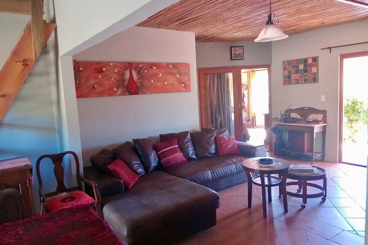 A rustic living room featuring terracotta floor tiles, a traditional thatched ceiling, and a wooden staircase leading to an upper level.