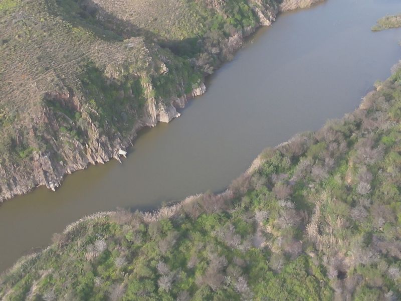 An aerial view of a river flowing through a natural landscape with rocky cliffs and surrounding vegetation.
